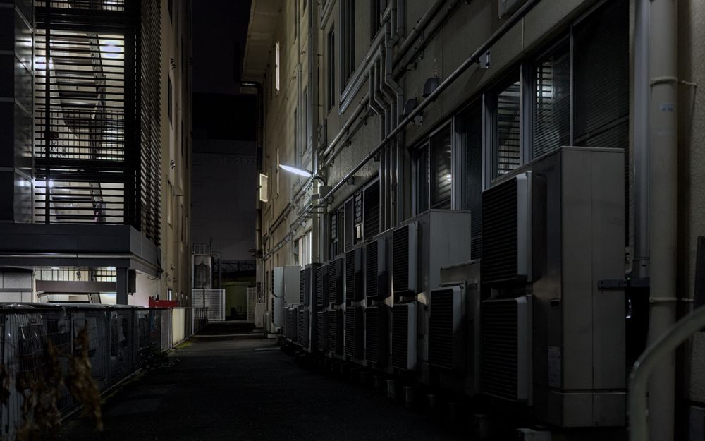 A dimly lit urban alley in Kyoto featuring air conditioning units, captured at night.