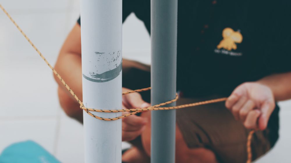 Close-up view of hands tying rope around two metal posts, showcasing knot craftsmanship.