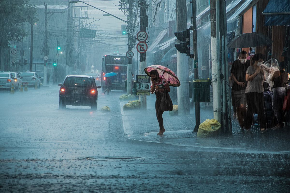 Heavy monsoon rain falling on a city street with people under umbrellas