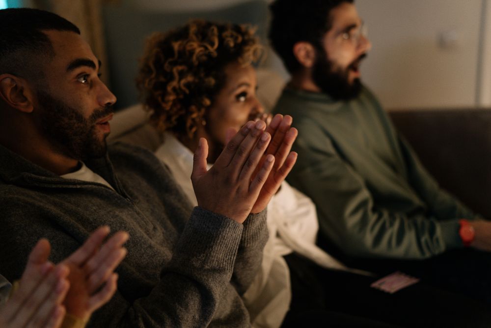 Diverse group of adults clapping with anticipation indoors, reflecting joy and engagement in a cozy setting.