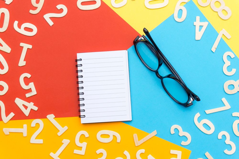 Vibrant flat lay featuring notebook, eyeglasses, and wooden numbers on colorful background.