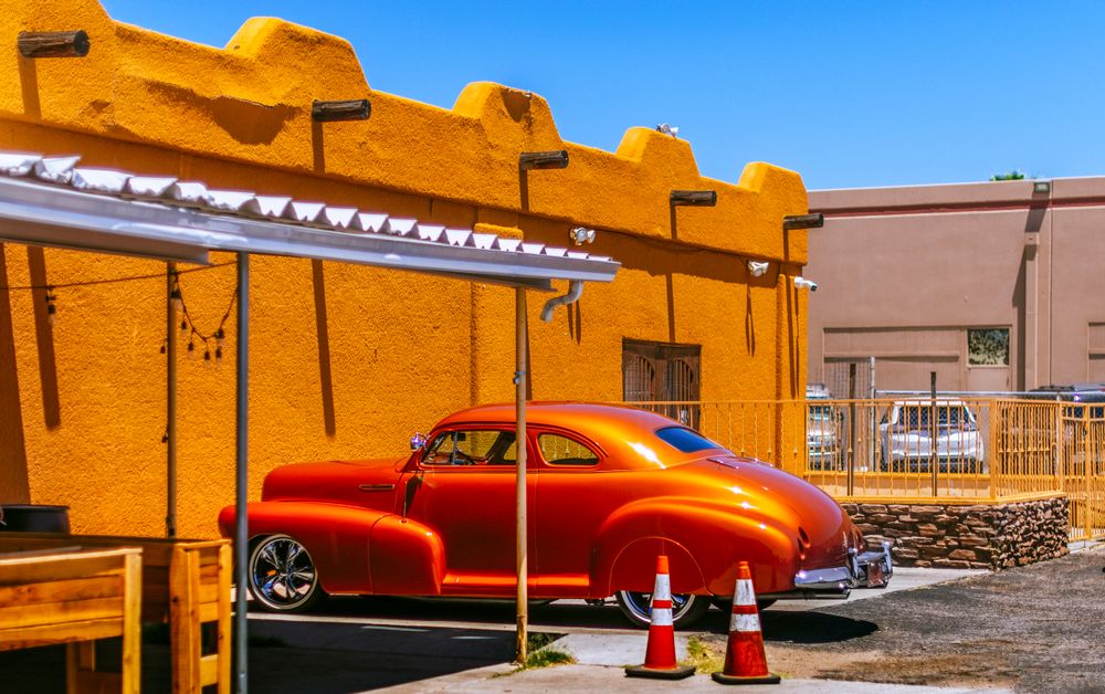 Vintage orange Chevrolet coupe parked by a vibrant wall in Tucson, Arizona.