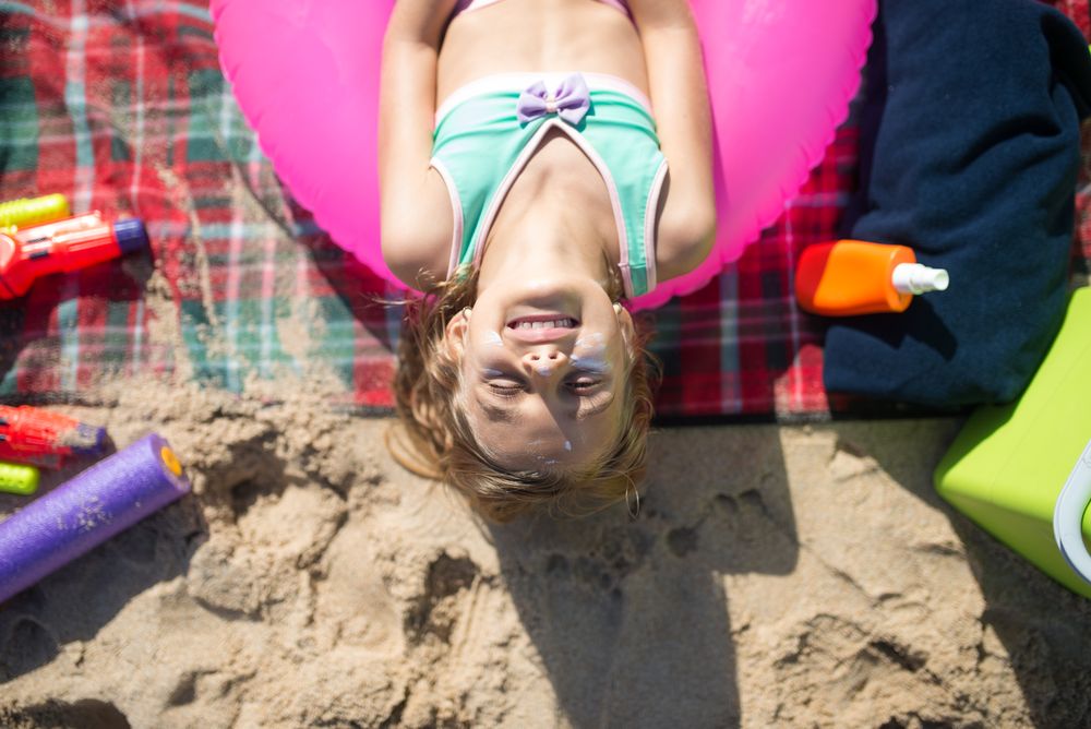 A young girl enjoying a sunny day on the beach with swimwear and sunblock.
