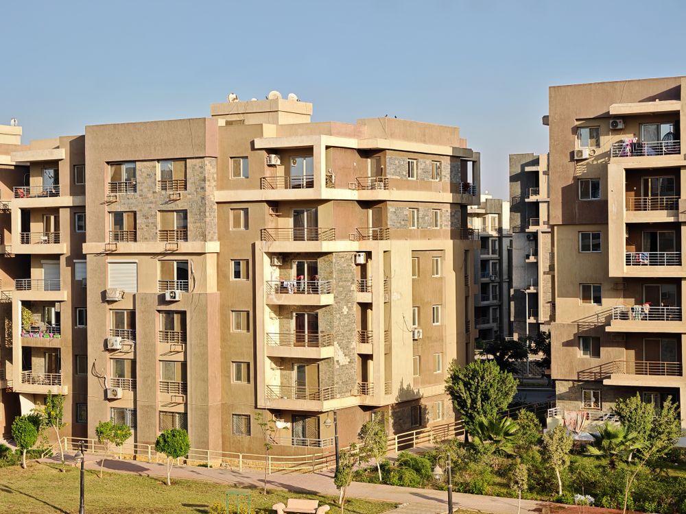 A modern apartment complex with multiple buildings in a sunny urban environment, showcasing contemporary architecture.