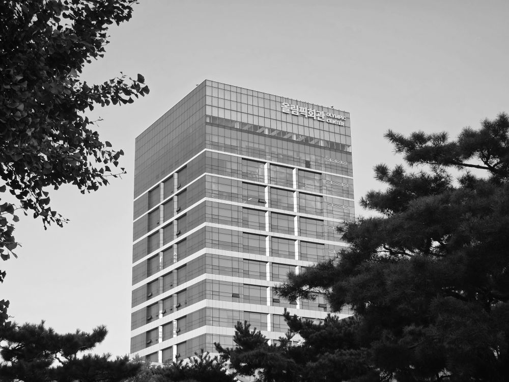 Black and white photo of Olympic Center building in Seoul framed by trees.