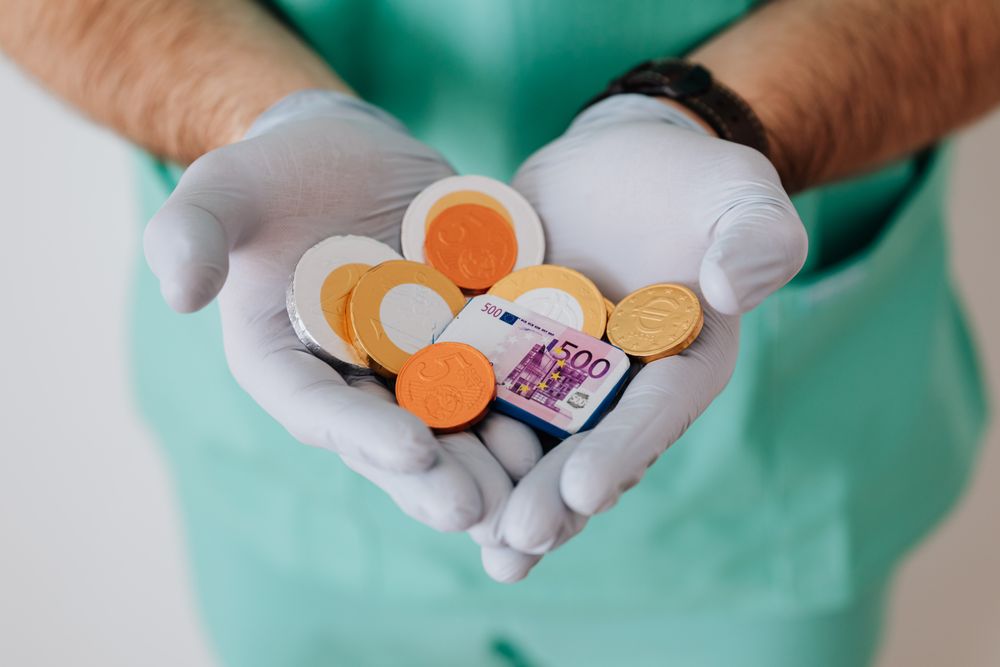 From above crop anonymous medical worker in rubber disposable gloves holding in hands chocolate coins