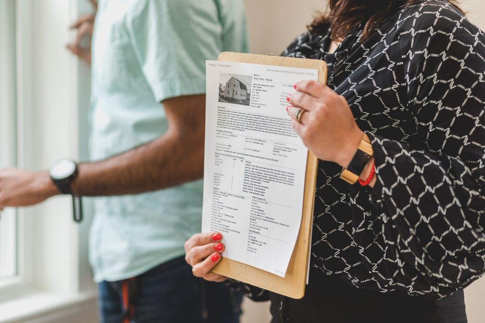 Real estate agent holding property documents on a clipboard in an office setting.