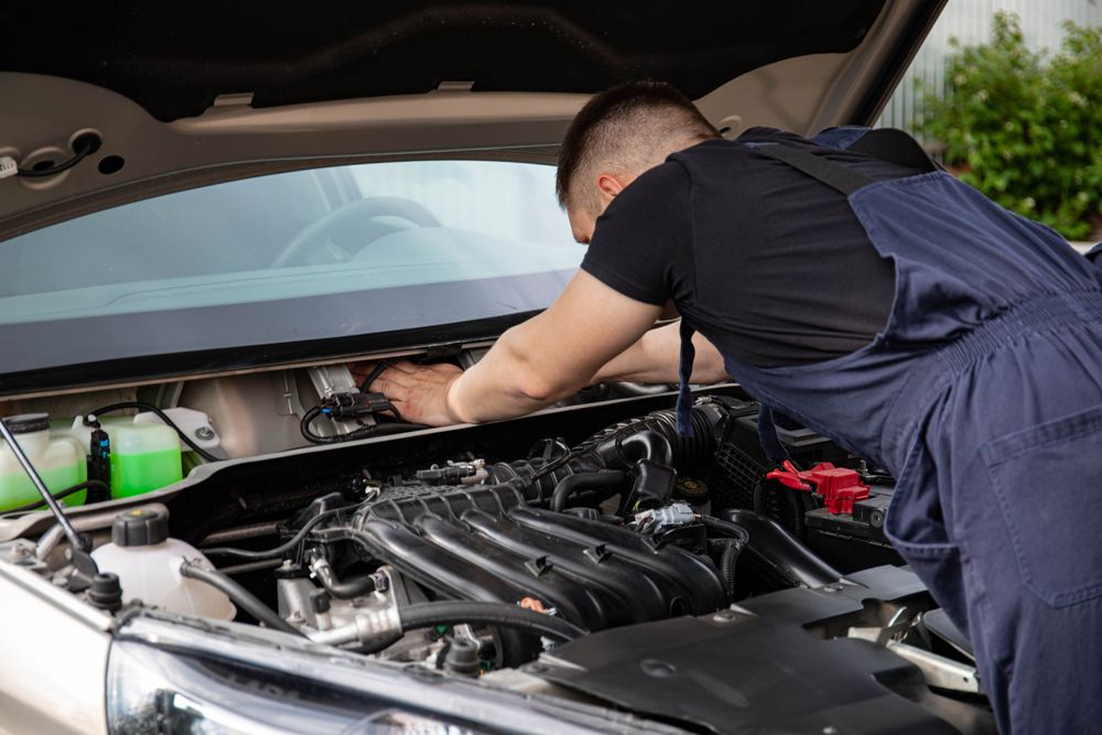 Auto mechanic performs engine maintenance on a car. Focus on hands and engine components.
