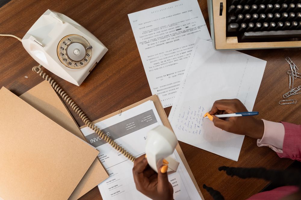 Overhead view of a person writing notes while holding a vintage telephone on a wooden desk.